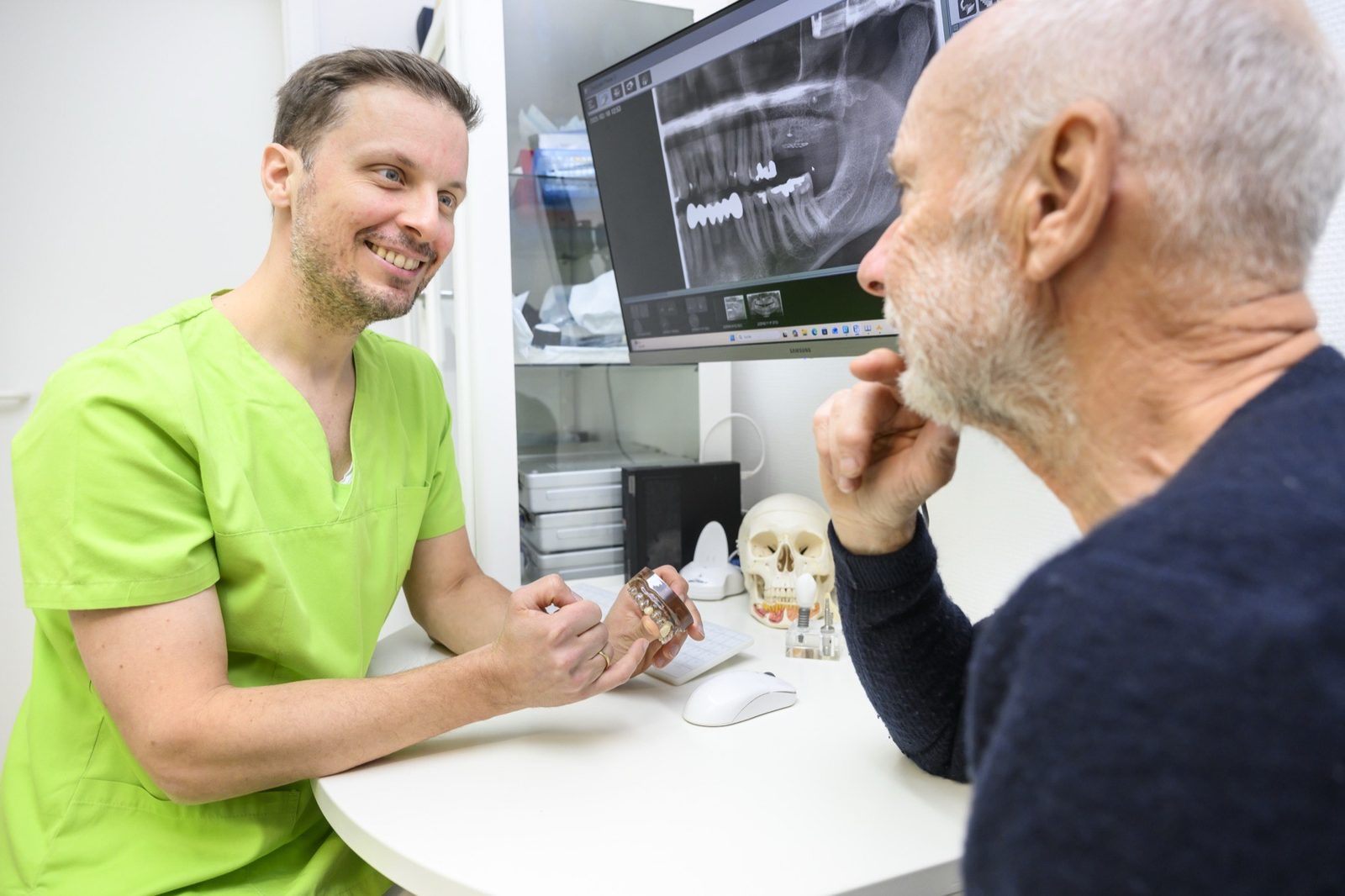 Dr. Ansgar Hergt erklärt einem Patienten die 3D-Aufnahme und ein Implantatmodell - Beratung in der Praxis Oralchirurgie & Implantologie Templin